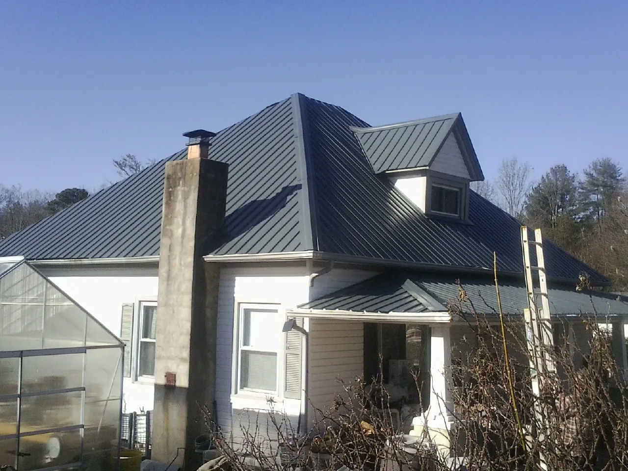 Dark blue standing seam metal roof on a white farmhouse with dormer — Slate & Tile Roof Repair by Roofing Brothers in Sabattus