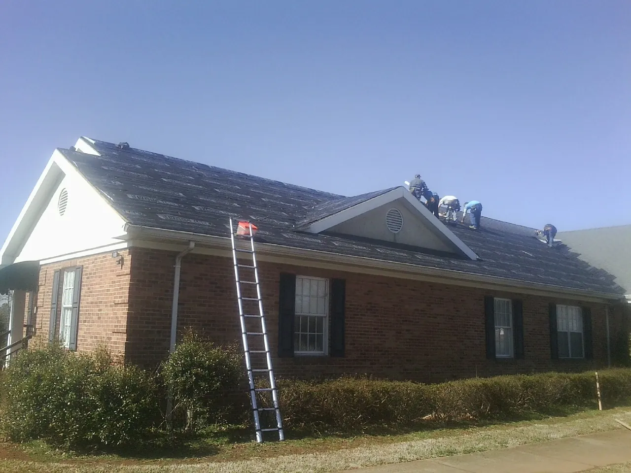 Crew tearing shingles off a brick ranch roof with a ladder set — Emergency Roof Repair work by our crew in Sabattus