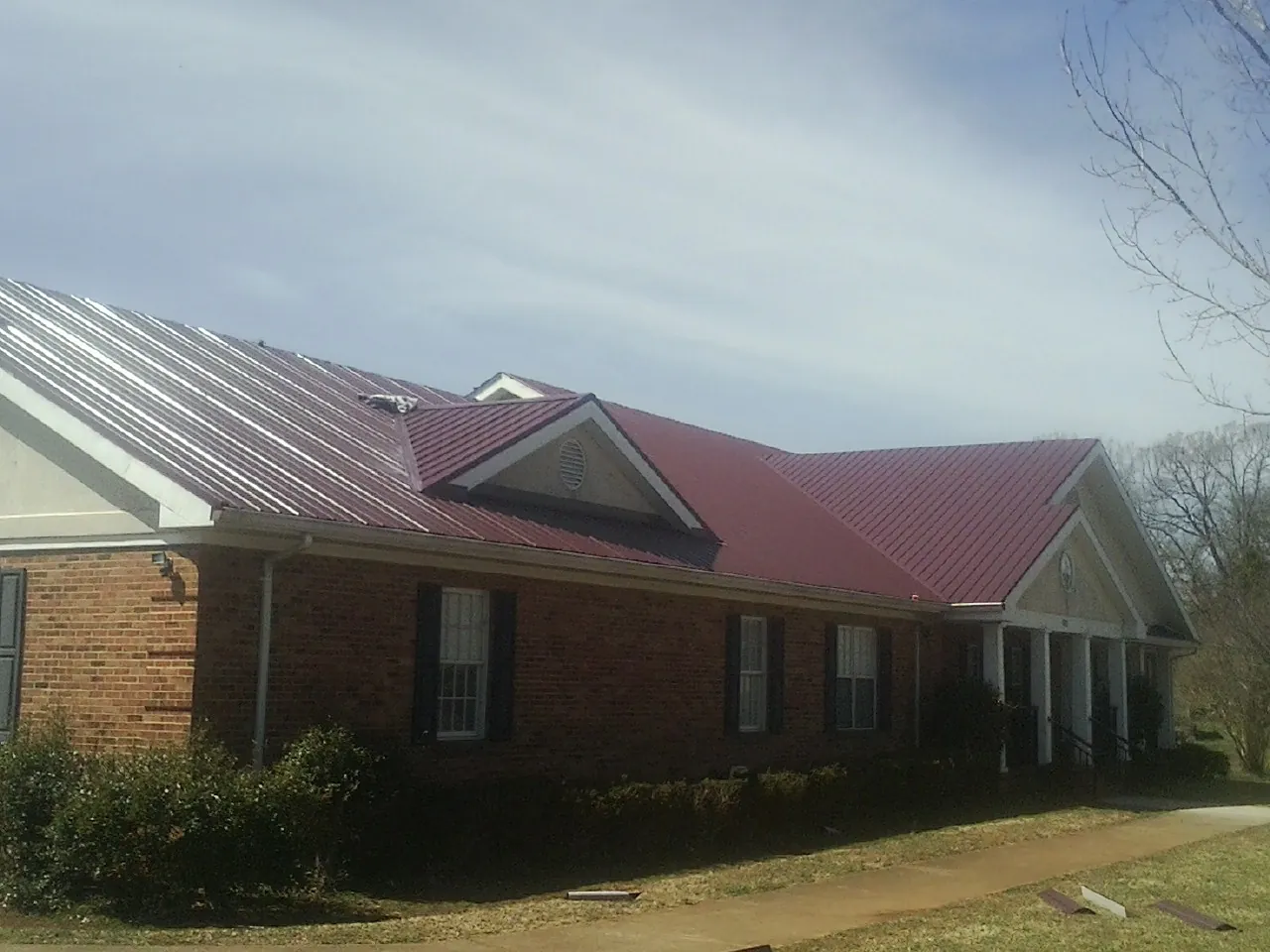 Red metal roof with gabled entries on a long brick building, from a Hail Damage Roof Repair job in Sabattus