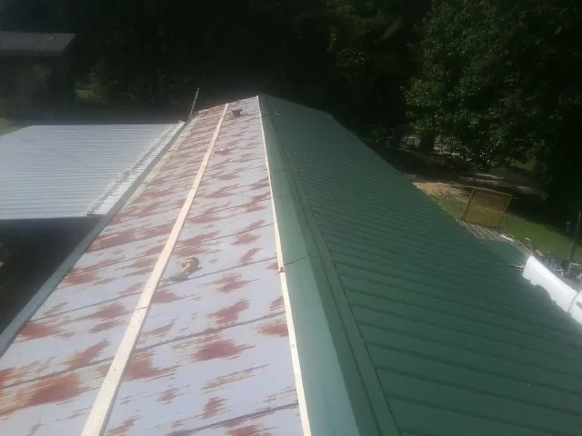Old rusted panels beside newly installed green metal roofing — Wind Damage Roof Repair by Roofing Brothers in Sabattus