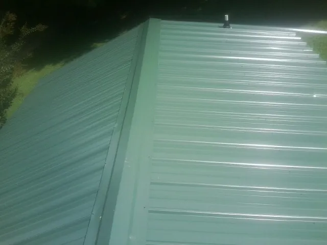New green metal panels meeting at the ridge of a roof — Flat Roof Repair work by our crew in Sabattus