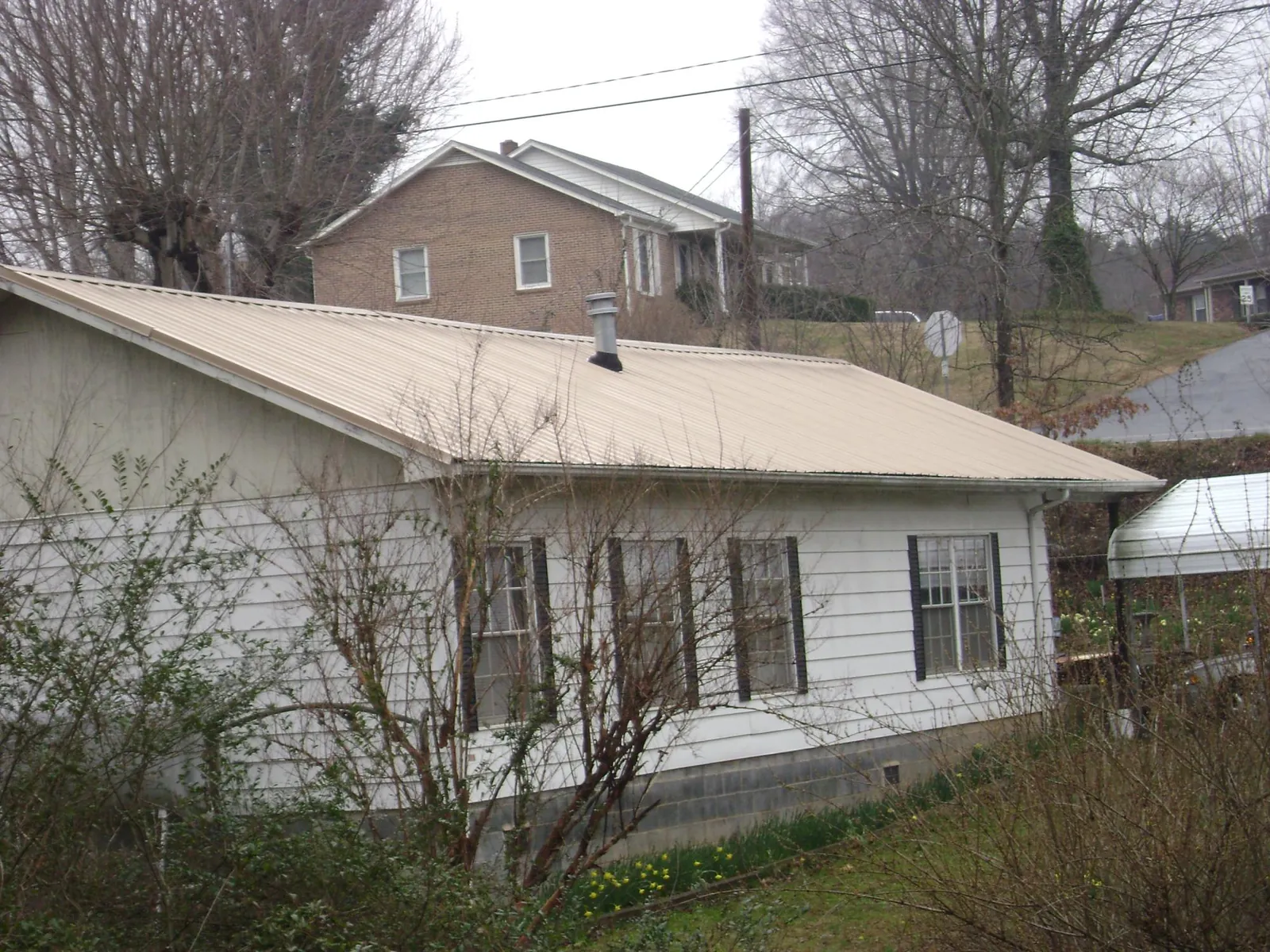 Tan metal roof on a white sided house set into a hillside — Commercial Roofing by Roofing Brothers in Sabattus