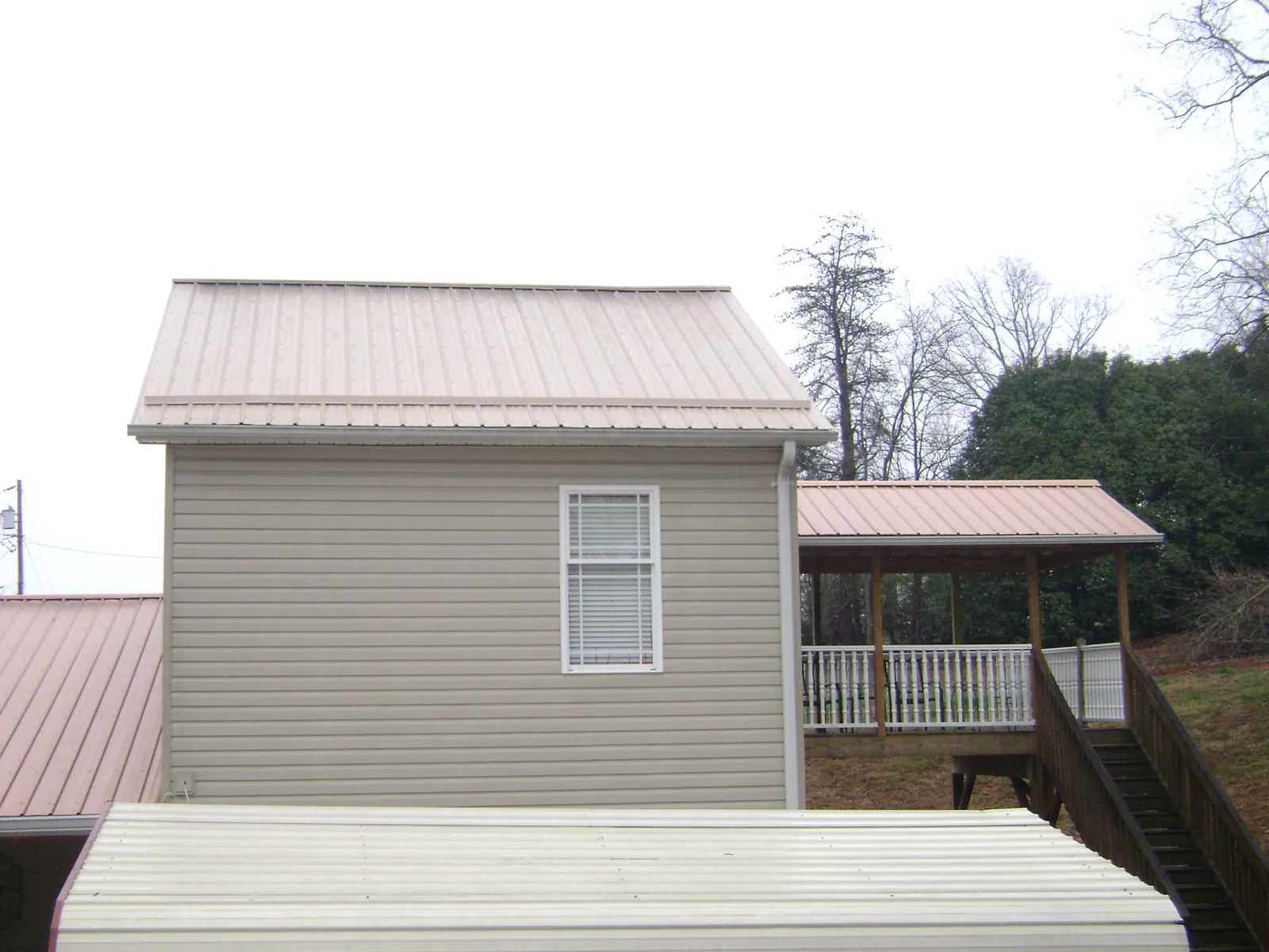 Tan metal roofs on a two story addition and attached porch, from a Roof Replacement job in Sabattus